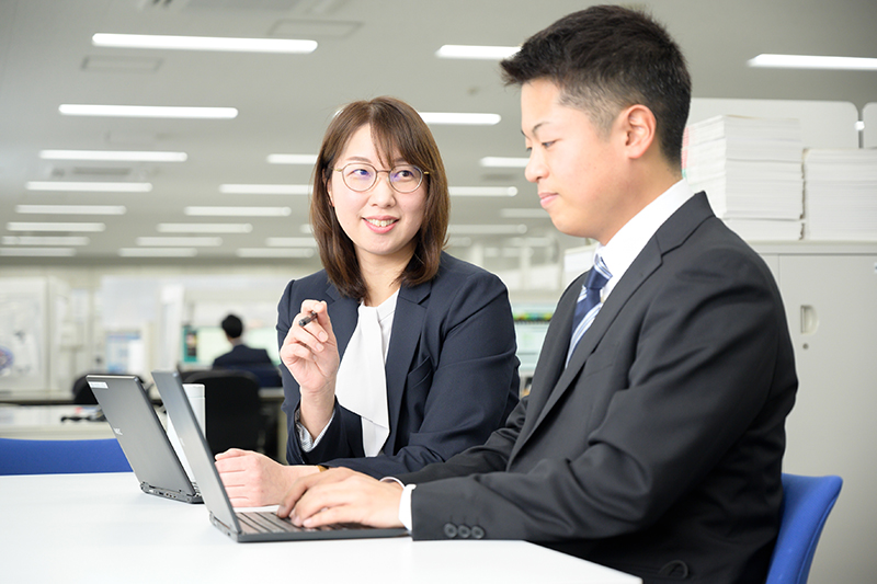 オフィスでパソコンを操作しながら男性と会話している女性